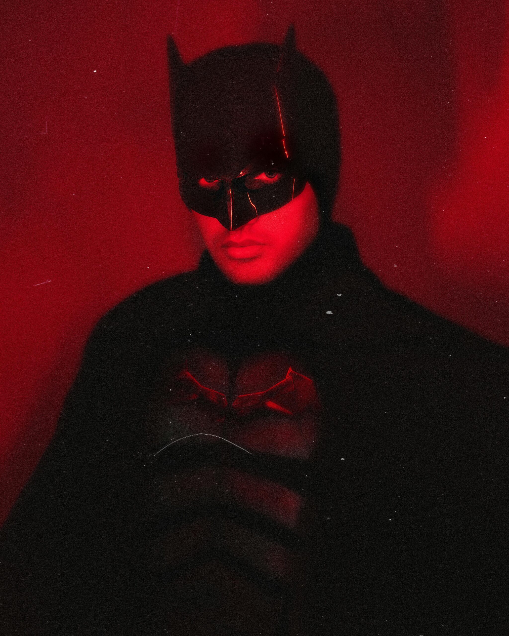 Person dressed as a dark masked superhero in dramatic red lighting.