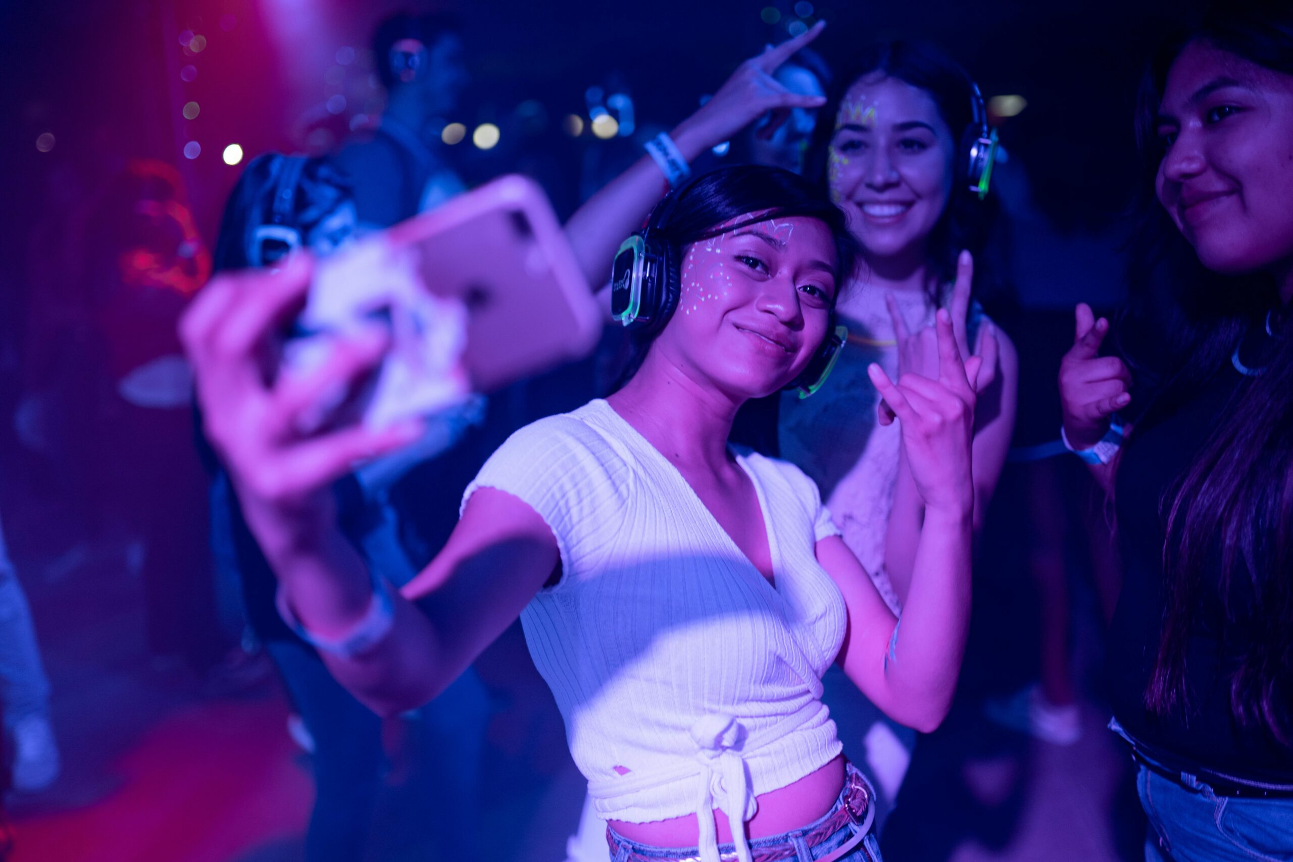 Teens wearing headphones taking a selfie on a dance floor with colorful lighting.