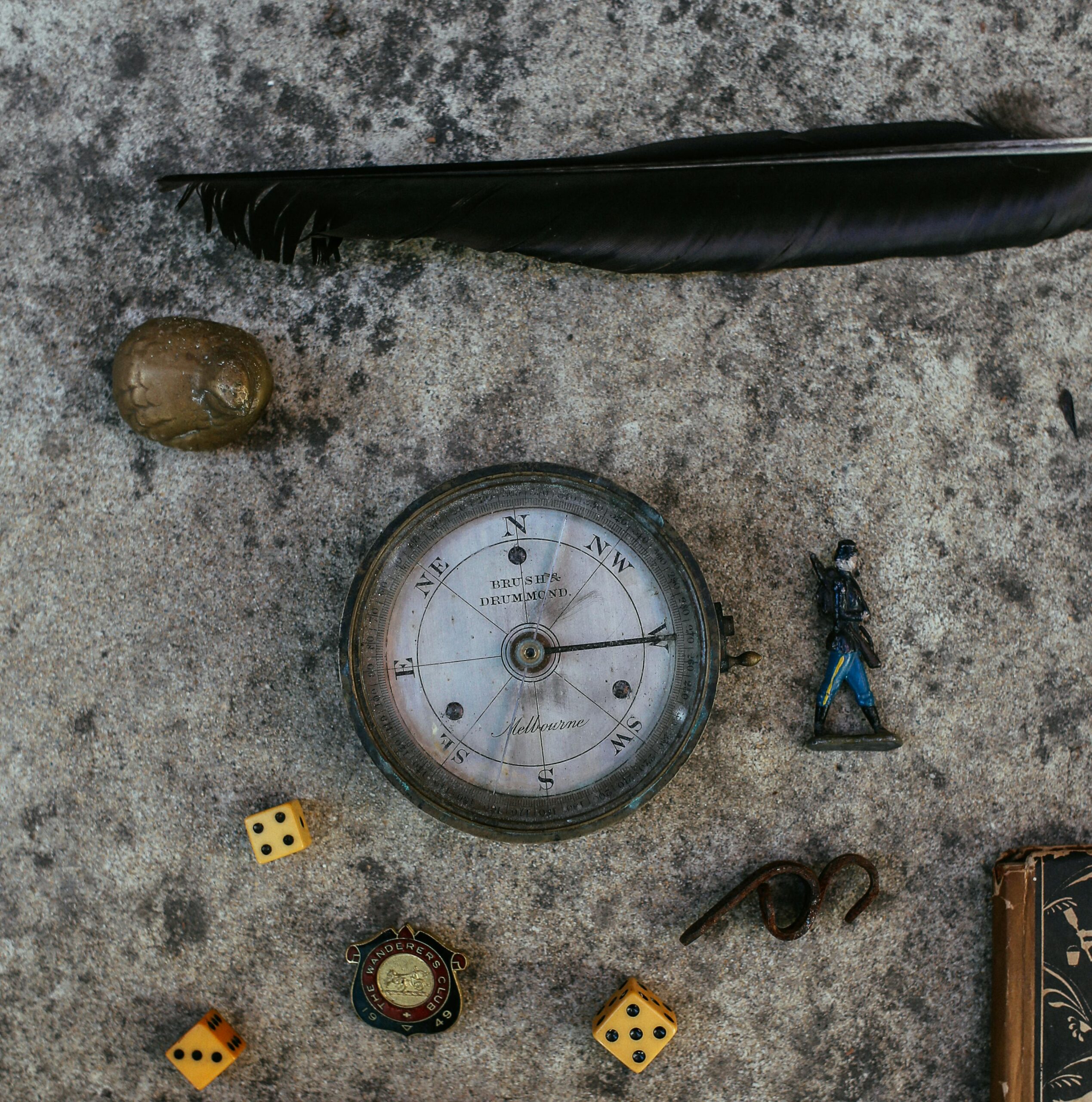 Flat lay of compass, dice, feather, toy soldier, and small objects on textured surface.