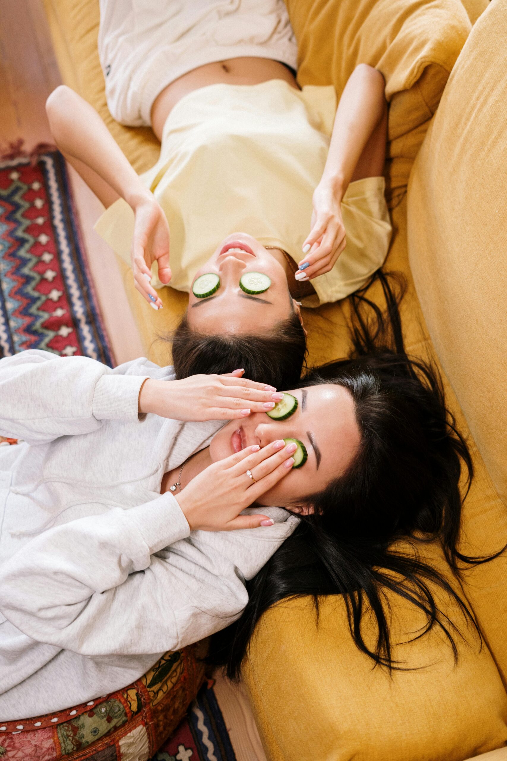 Two girls relaxing on a couch with cucumber slices over their eyes during spa time.
