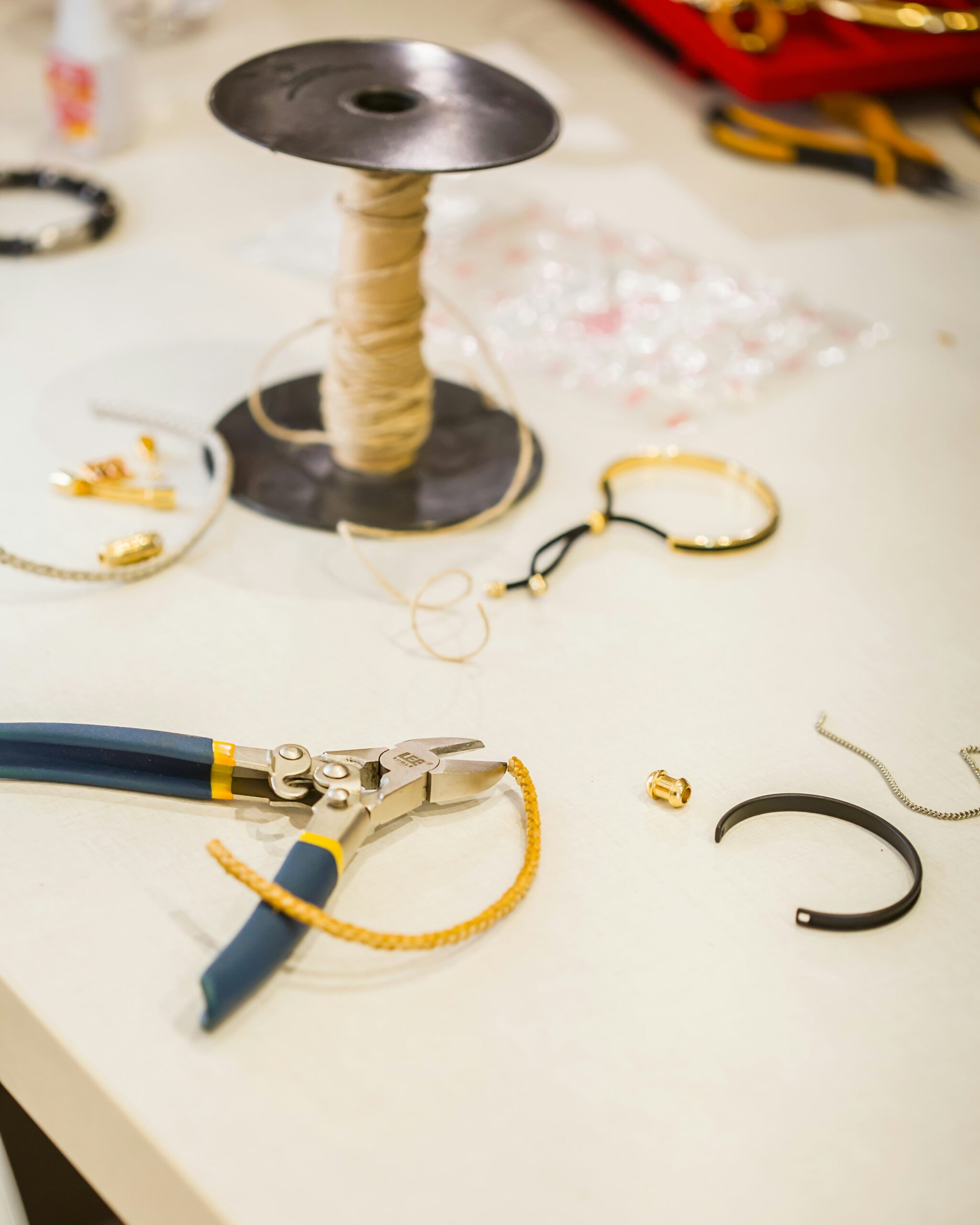 Jewelry-making tools and supplies spread on a table with pliers and string spool.