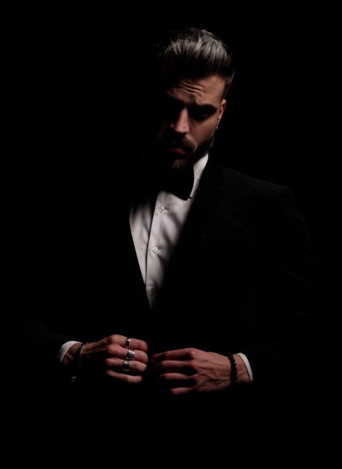elegant fashion man closing black velvet tuxedo and posing in a fashion light on black background in studio