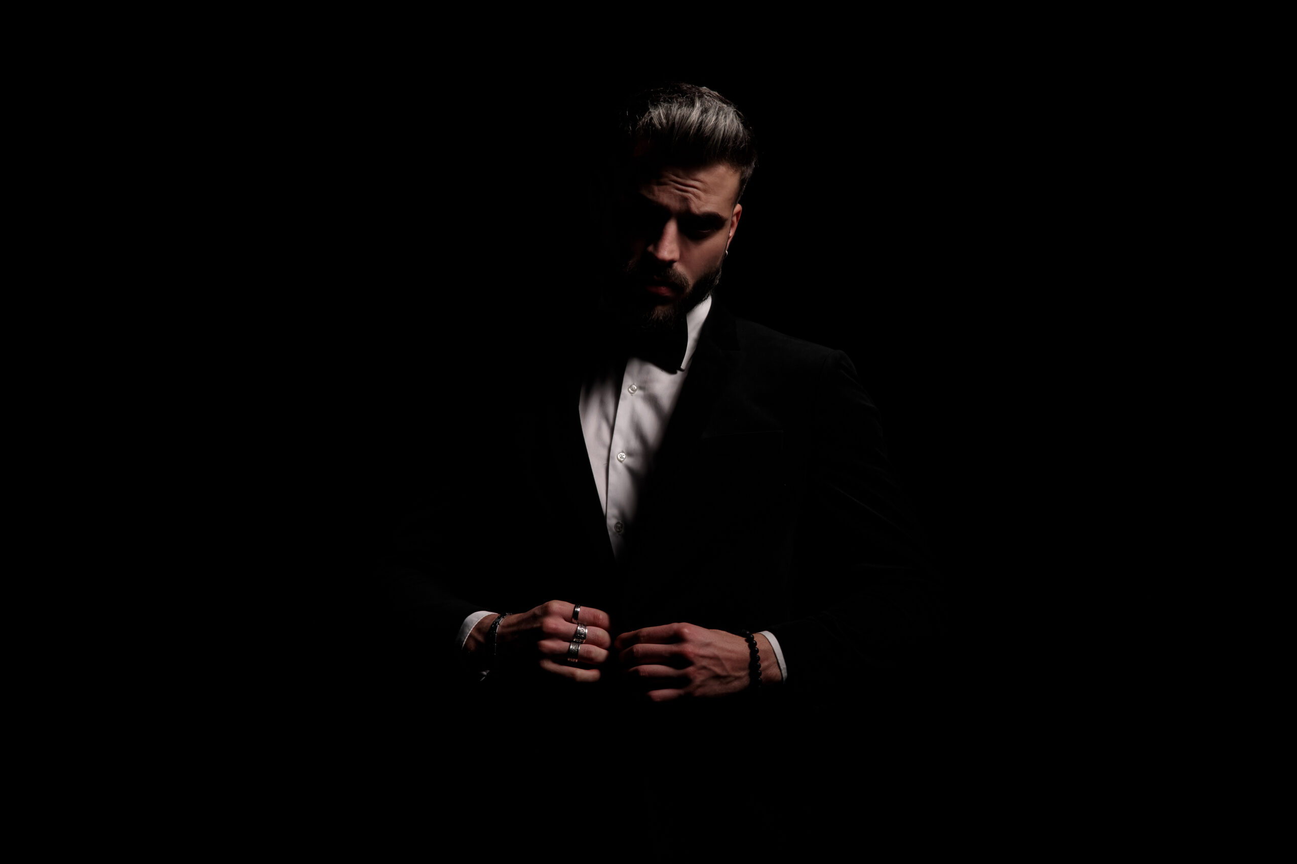 elegant fashion man closing black velvet tuxedo and posing in a fashion light on black background in studio