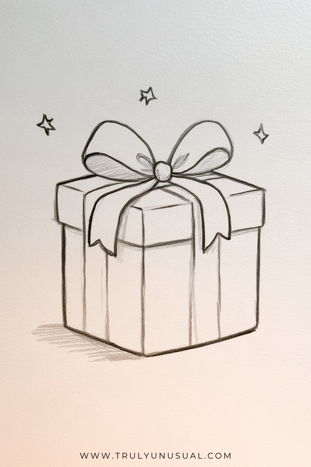 Cute and easy Christmas present pencil drawing featuring a square gift box wrapped with wide ribbons and topped with a large decorative bow. Three small hand-drawn stars sparkle above the present, adding a festive touch. The black and gray graphite sketch features clean outlines, gentle shading, and a simple three-dimensional design on textured white paper, perfect for Christmas drawing inspiration for kids and beginners.